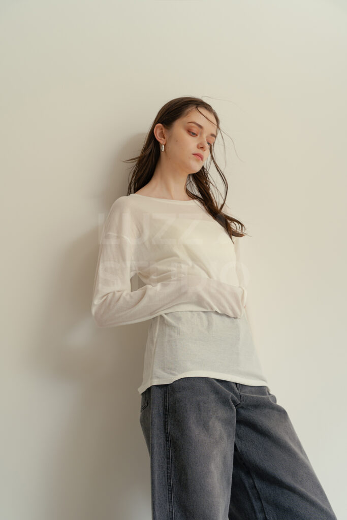 白壁にもたれる女性モデルにたなびく風を演出したSNSや広告向けレディスアパレル撮影写真