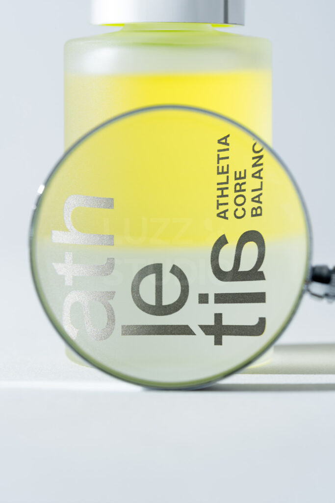 虫眼鏡の歪みを活かしてロゴを大胆に捉えた、グラフィカルなスキンケア商品の広告撮影事例。2層のオイルバルクの美しさとタイポグラフィを融合させた、アイキャッチの強いビジュアル訴求。