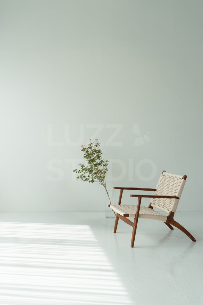 明るい白壁の前に置かれたペーパーコード編みの木製イージーチェア。床に落ちるカーテン越しの自然光が美しい、清潔感あふれる大阪のスタジオ内装