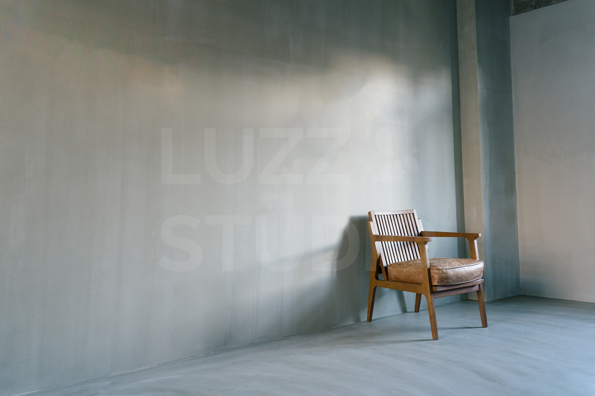 大阪の撮影会社によるスタジオ撮影サービス。質感のあるグレーのモルタル壁を背景に、ヴィンテージチェアと柔らかな自然光を活かした、洗練されたポートレート・広告撮影
