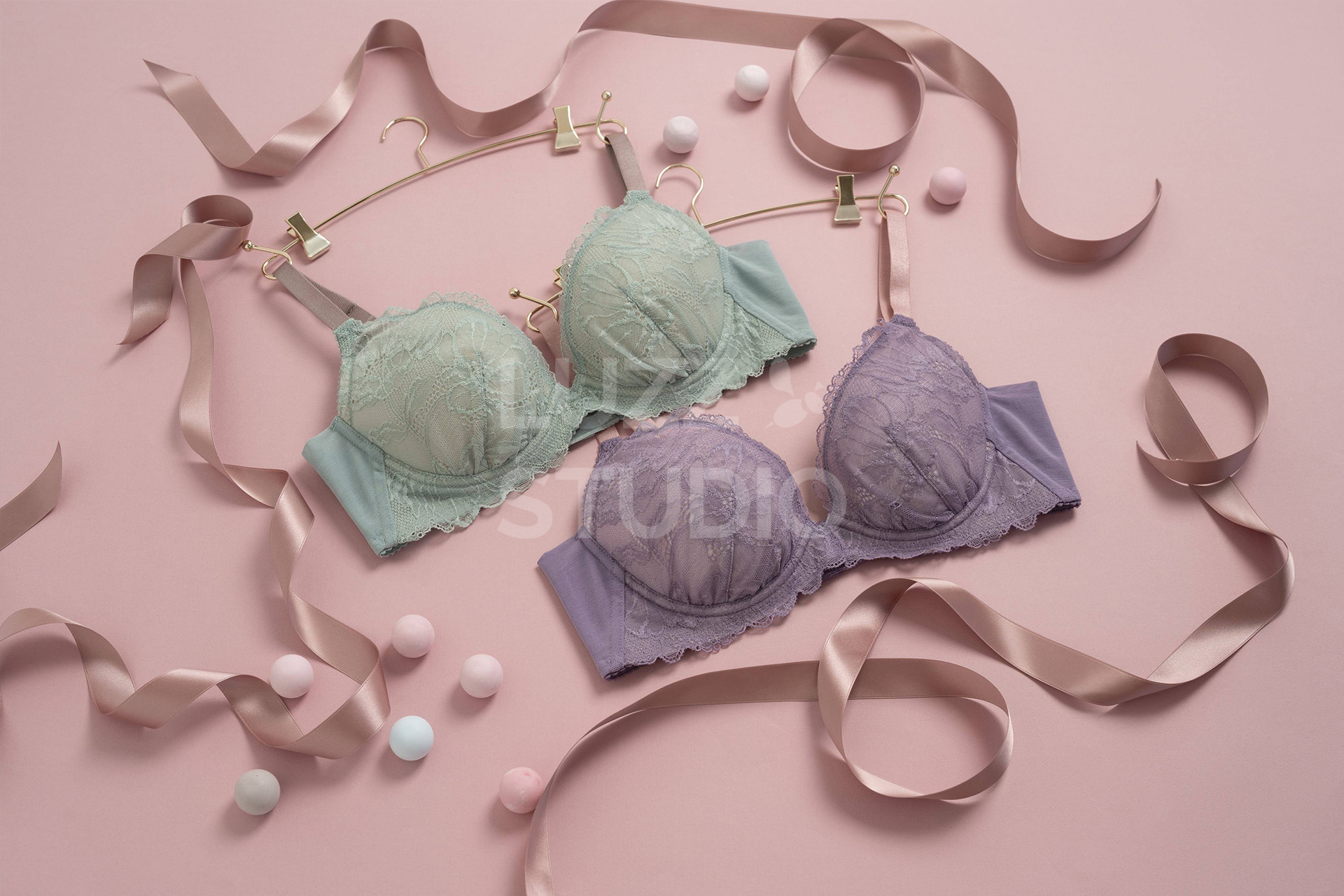 ピンクの背景紙の床の上にミントグリーンとパープルのブラジャーを配置した商品撮影写真。リボンやゴールドのハンガーを用いて女性への贈り物、自分へのご褒美といった、ギフト商材としての訴求もしている写真