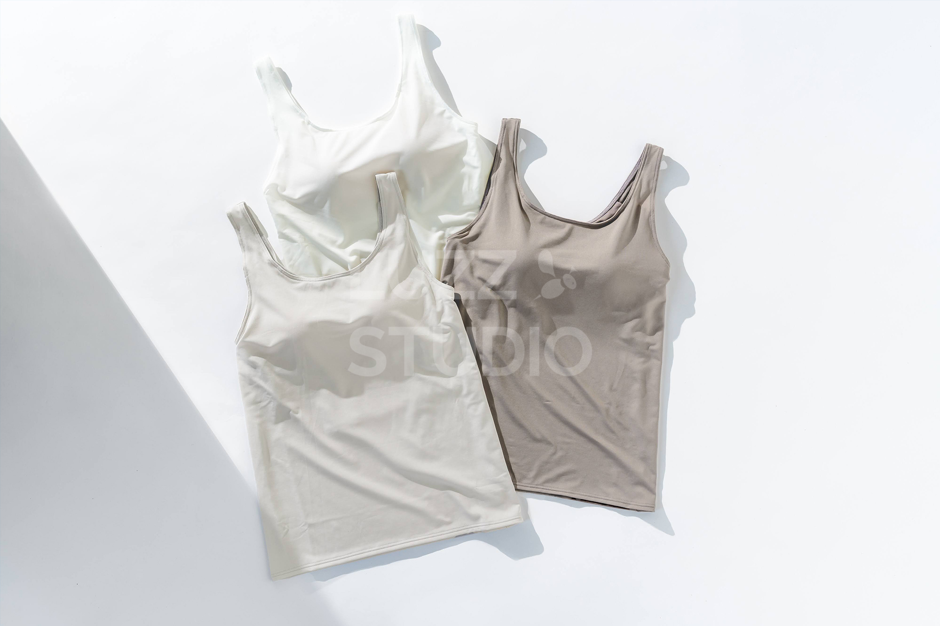 白背景の床の上にホワイトとブラウンとベージュのブラトップを配置した商品撮影写真。斜めの影によって、メリハリをつけている写真に仕上げている