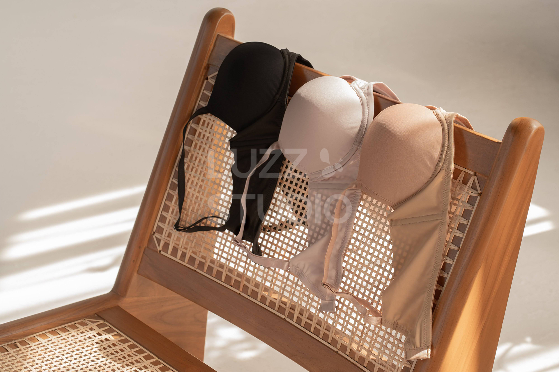 ローチェアのダイニングチェアの背もたれに、ブラックとピンクとベージュのブラジャーがかけられている商品撮影写真。ラタンチェアのデザイン性と相まった窓からの自然光の光の筋が、憧れの生活スタイルを演出し、興味惹かれるビジュアルに仕上げている