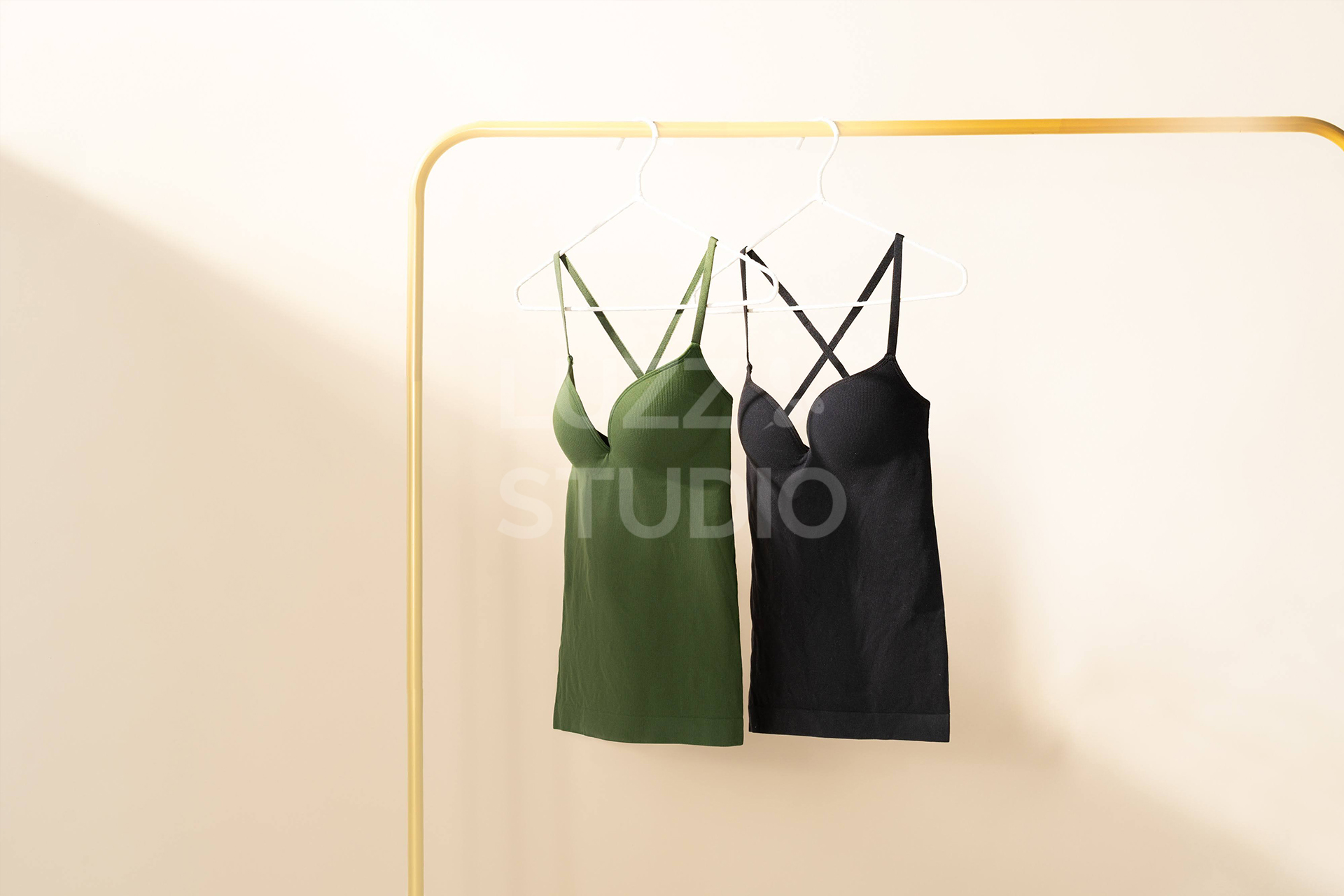 ゴールドのハンガーラックにグリーンとブラックのブラトップ（キャミソールタイプ）をハンガーにかけて配置した商品撮影写真。朝の陽ざしを彷させる強めの光の差し込む背景によって、商品にフォーカスするように工夫された写真