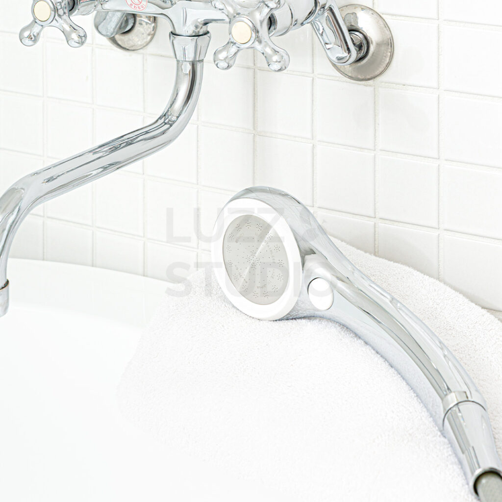 商品撮影:白タイル壁の浴室にある浴槽の淵に置いたウェブサイト・販促用のシャワーヘッド