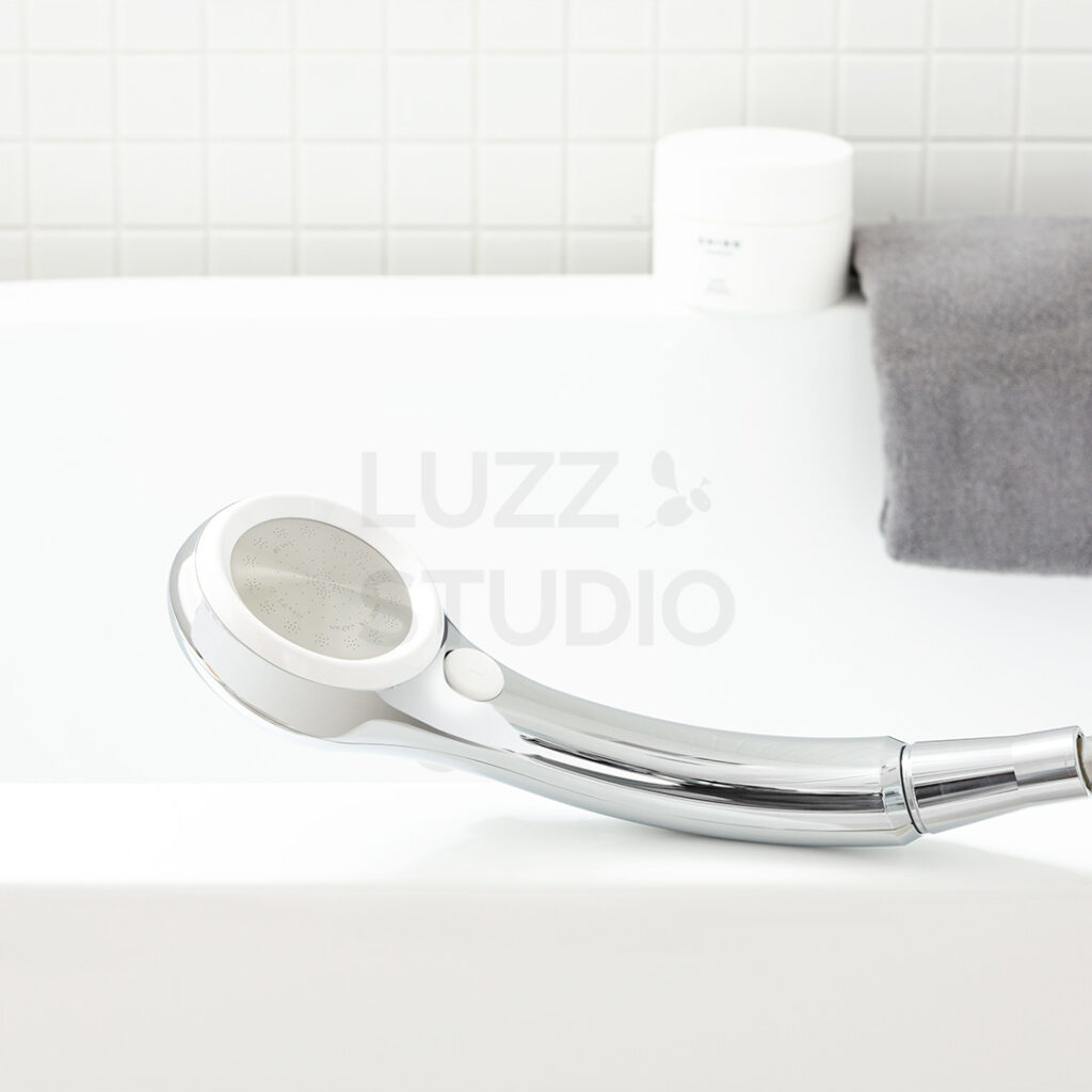 商品撮影:白タイル壁の浴室にある浴槽の淵に置いたウェブサイト・販促用のシャワーヘッド