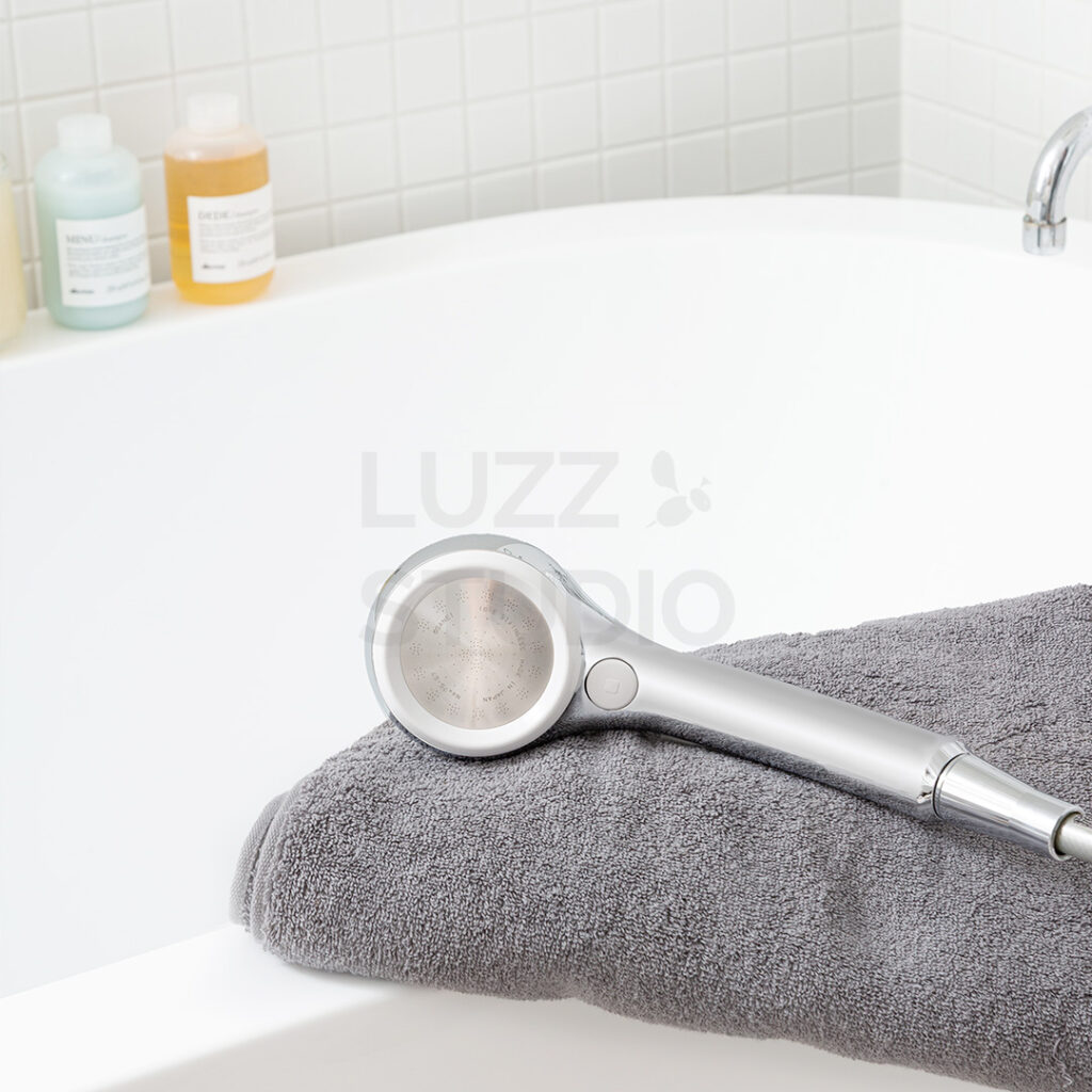 商品撮影:白タイル壁の浴室にある浴槽の淵にタオルと一緒に置いたウェブサイト・販促用のシャワーヘッド