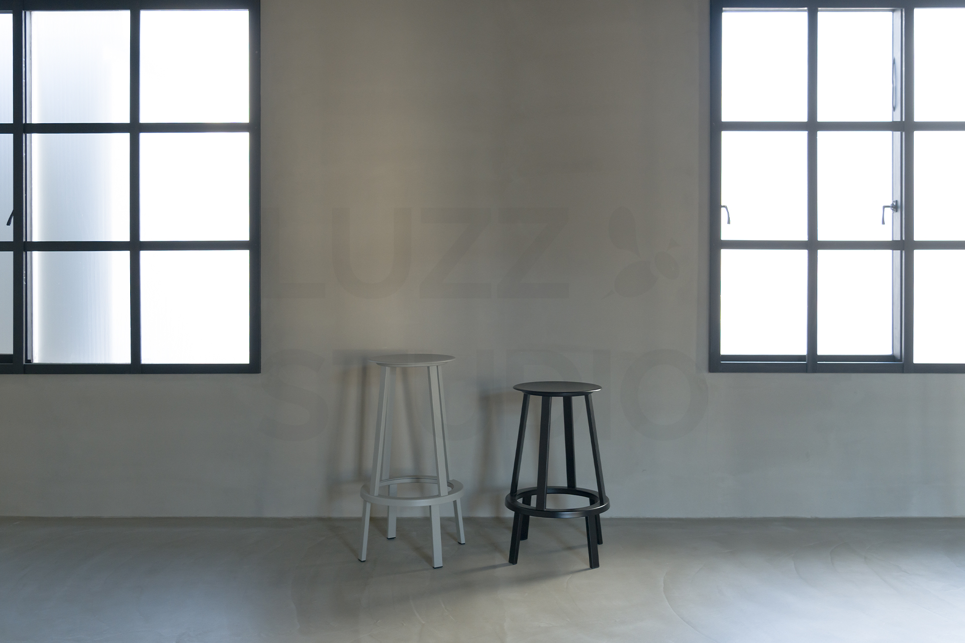 大阪の撮影スタジオ。2面の格子窓から自然光が差し込むグレーモルタル壁の撮影エリア。モノトーンのハイスツールを配したモダンで無機質な空間