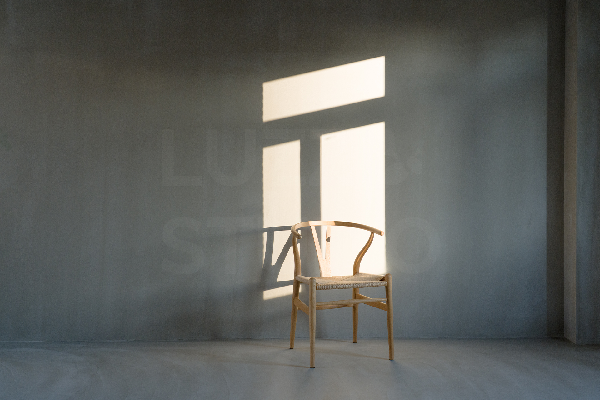 大阪の撮影会社がプロデュースする、グレーのモルタル壁と自然光のコントラストを活かしたスタジオ撮影。Yチェアを配したモダンな空間で、洗練されたポートレートや広告写真の撮影を承ります