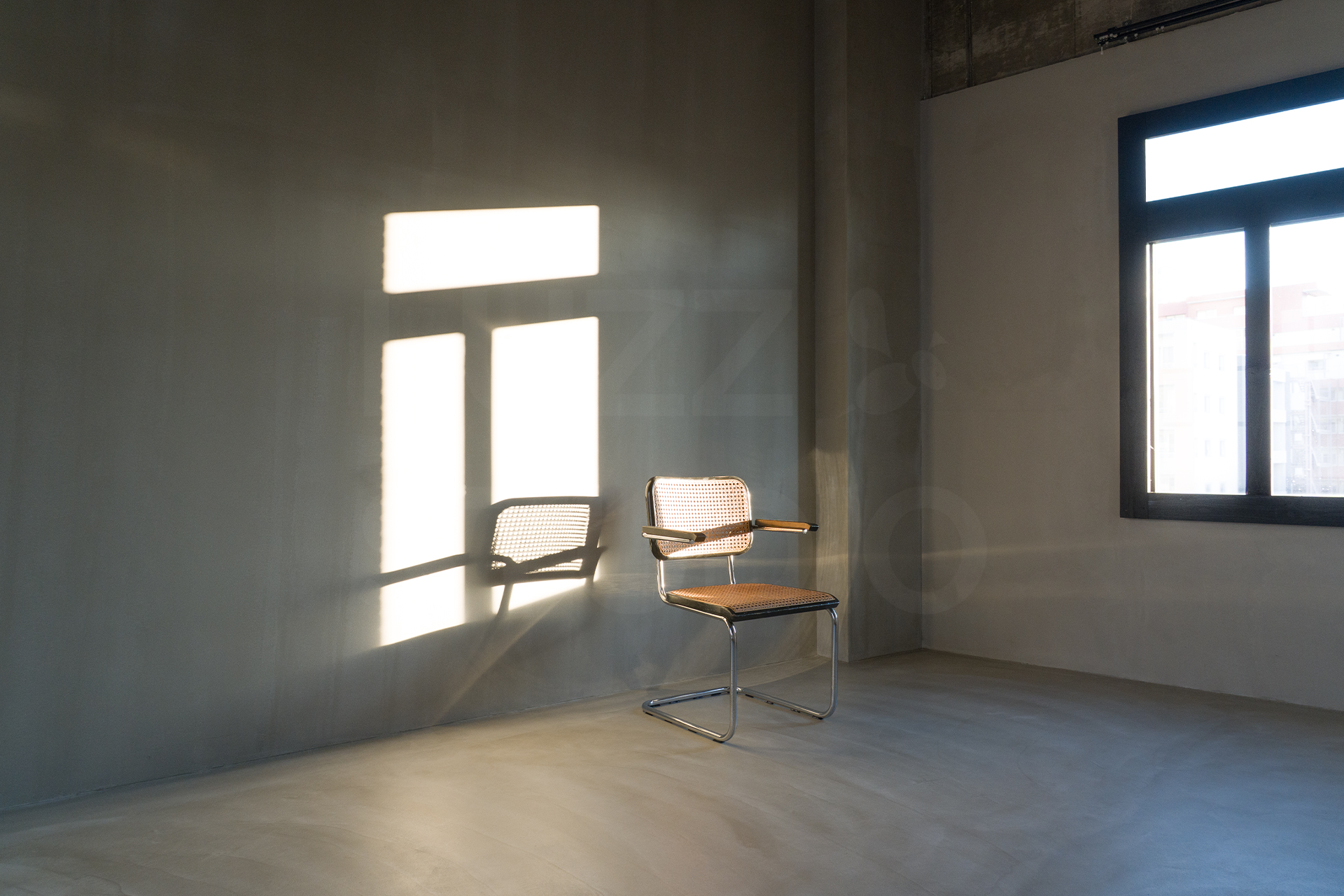 大阪の撮影会社によるスタジオ撮影サービス。グレーの壁に差し込む印象的な自然光と名作家具を組み合わせた、ドラマチックなポートレートや広告写真の撮影イメージ