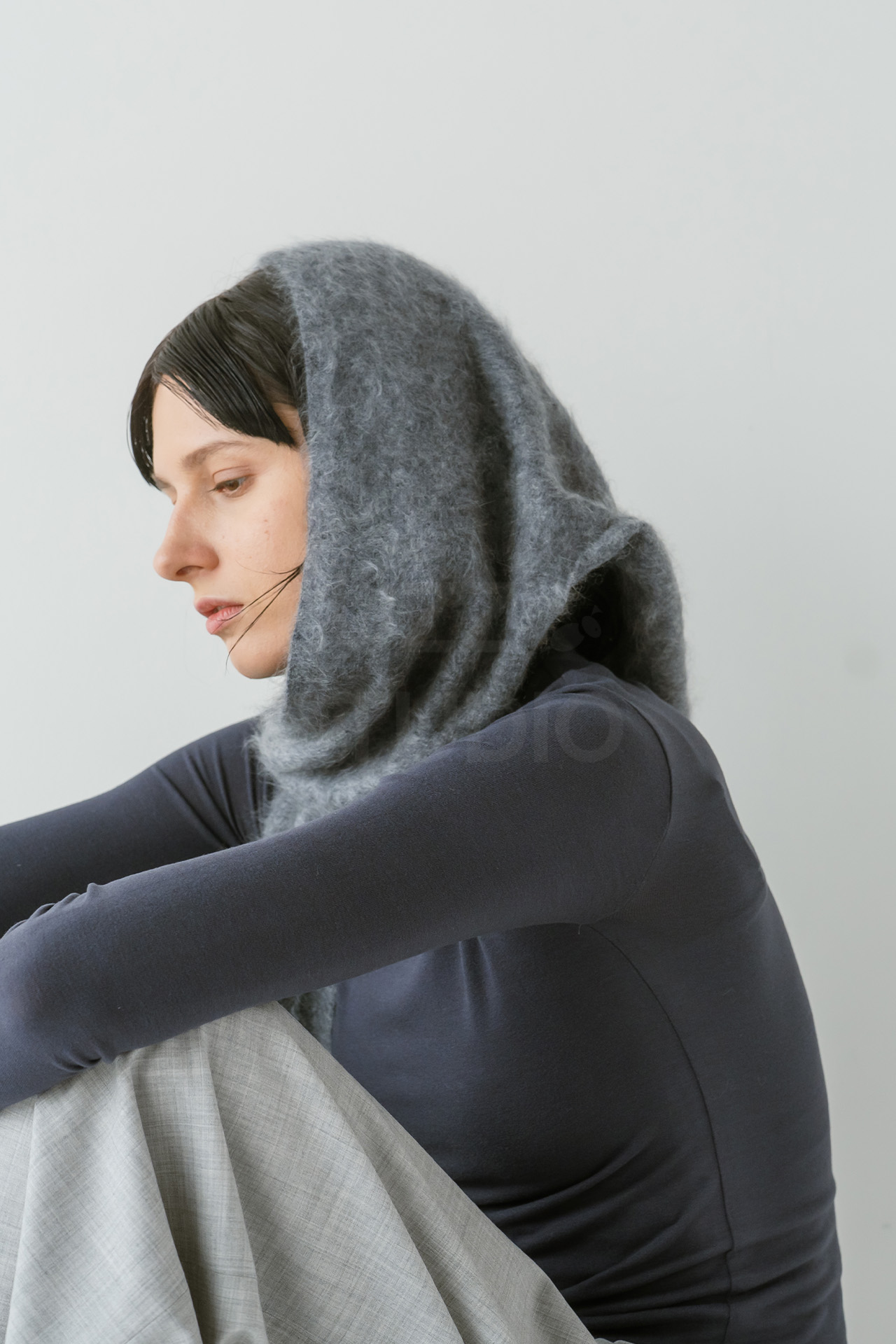 ダークネイビーのトップスの上からグレーのモヘア調ストールを頭部に巻き付け、横を向いて座るモデルのポートレート風写真