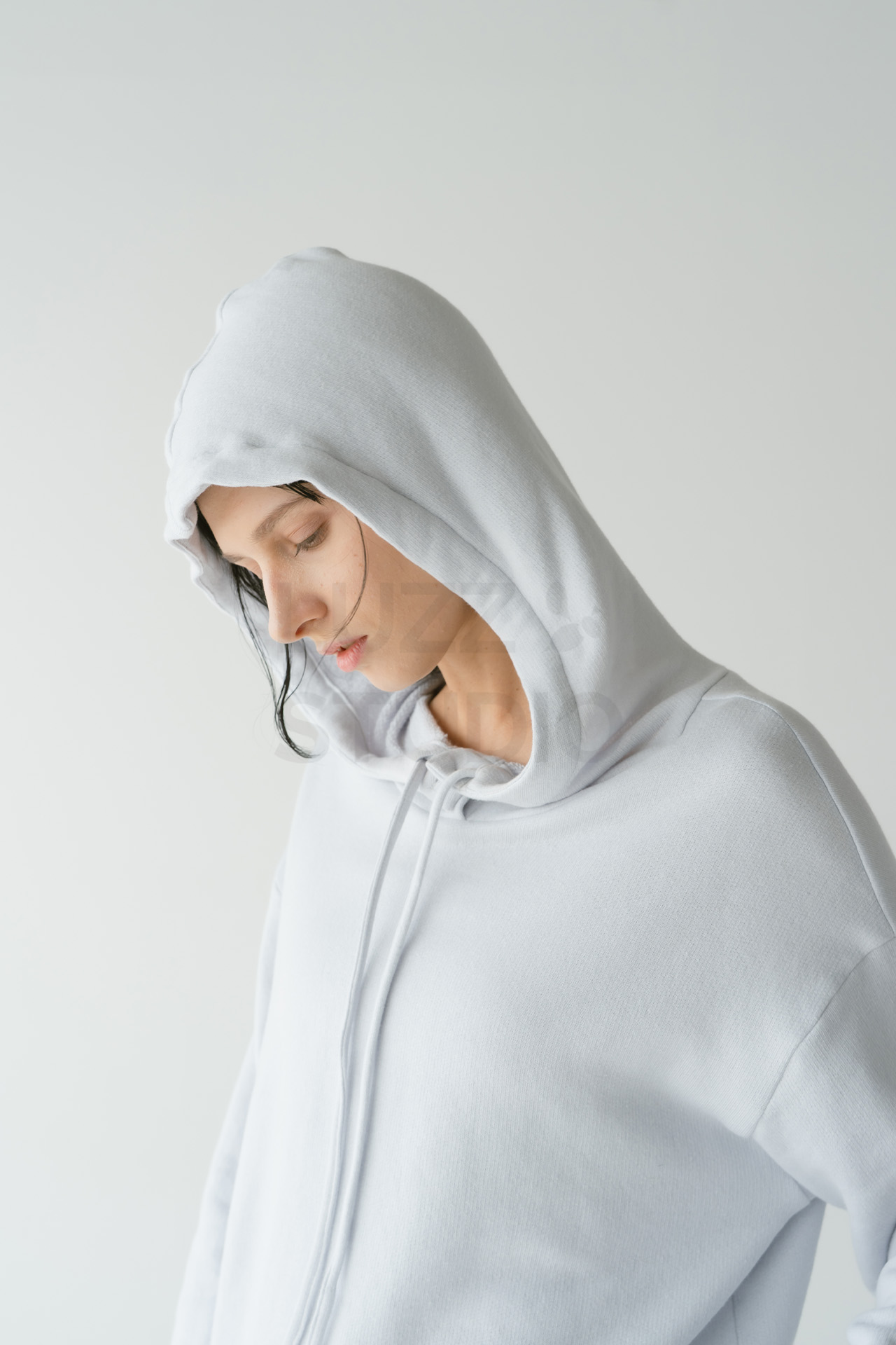 薄いグレーのフード付きパーカーを着用し、少し下を向いた自然な表情を捉えたモデルのクローズアップ写真。