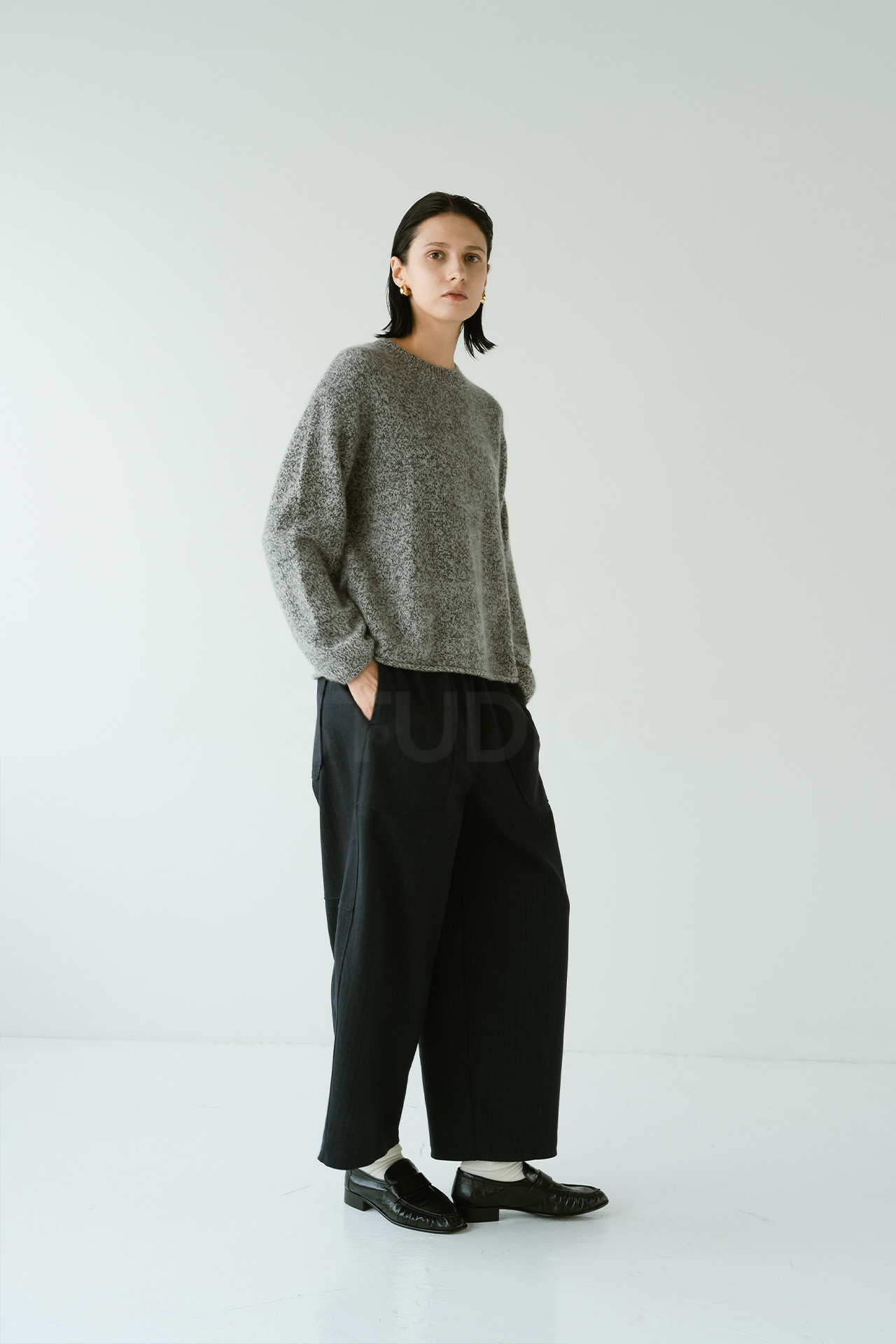 杢グレーのニットに黒のワイドパンツ、ローファーを合わせたシンプルなスタイリングでポケットに手を入れて立つモデルの全身ショット