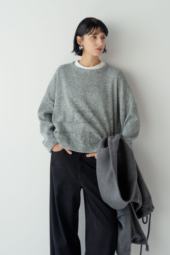 グレーのニットに黒のパンツを合わせ、アウターを片手に持って自然な動きを見せたコーディネートショット