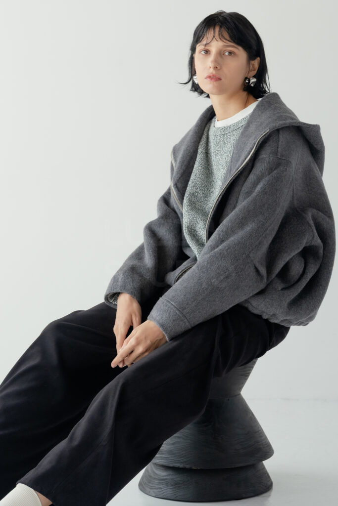 スツールに腰掛け、リラックスしたポーズでグレーのジャケットとパンツの質感を際立たせた全身ショット