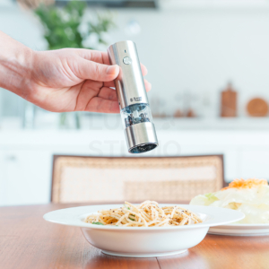 電動ミルの使用シーン・調理動作の撮影事例。ダイニングテーブルで料理にスパイスを挽きかける手元を捉え、商品のサイズ感と利便性をリアルに再現した物撮りカット