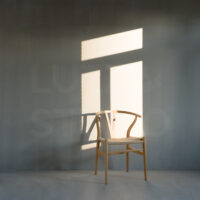 大阪の撮影会社がプロデュースする、グレーのモルタル壁と自然光のコントラストを活かしたスタジオ撮影。Yチェアを配したモダンな空間で、洗練されたポートレートや広告写真の撮影を承ります